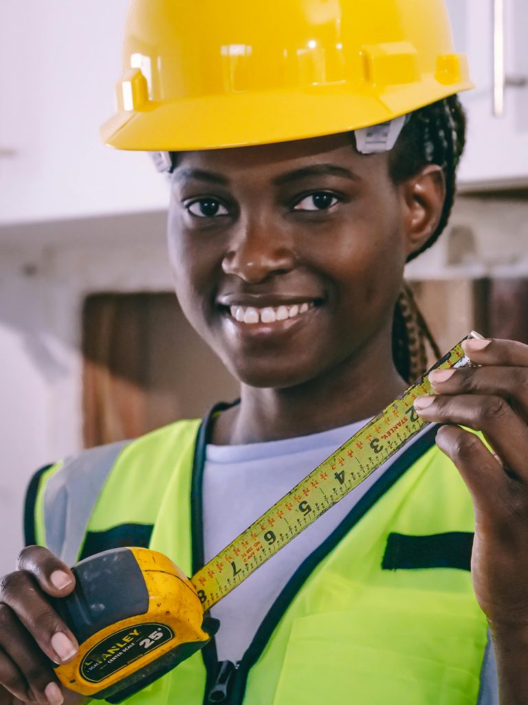 Cheerful female engineer wearing PPE and holding a measuring tape indoors.